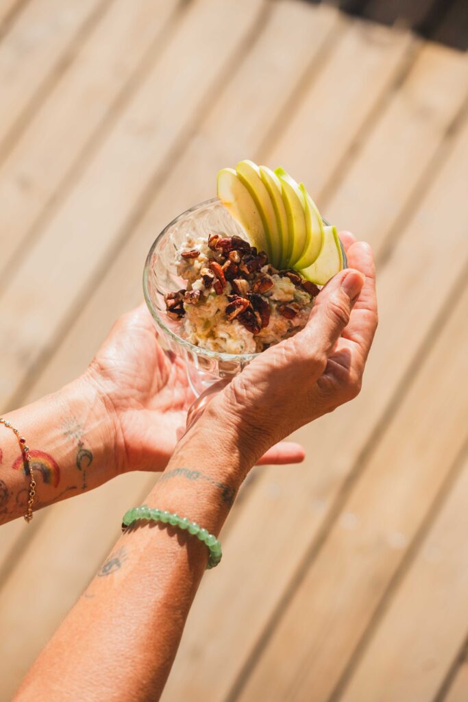 Hands holding a glass of granola, yoghurt and fresh apple on the sunlit rooftop deck